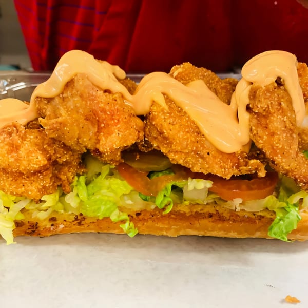 A close-up of Noonie’s Place fried shrimp po'boy with lettuce, tomato, pickles, and sauce.