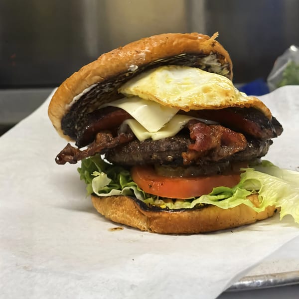 A Noonie's Place soul-food burger with a fried egg, bacon, cheese, lettuce, and tomato.