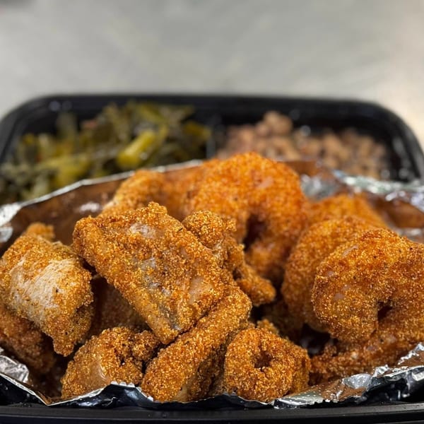 Noonie's Place soul food meal with crispy fried fish, collard greens, and beans in a black container.