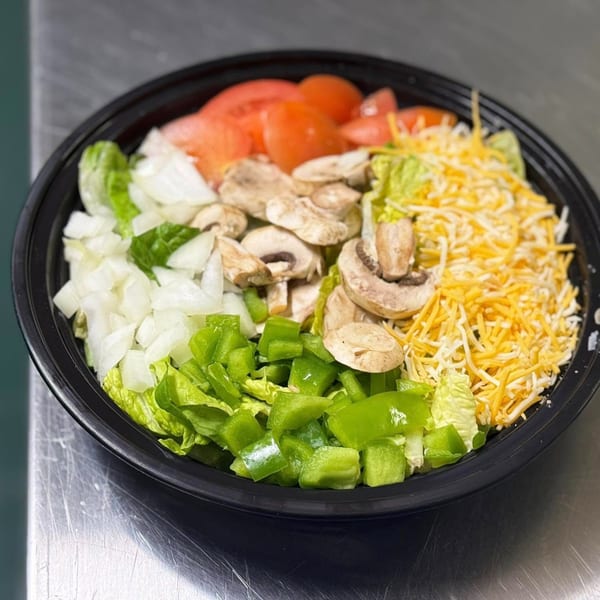 A black bowl filled with fresh salad ingredients: tomatoes, mushrooms, onions, green peppers, lettuce, and shredded cheese.