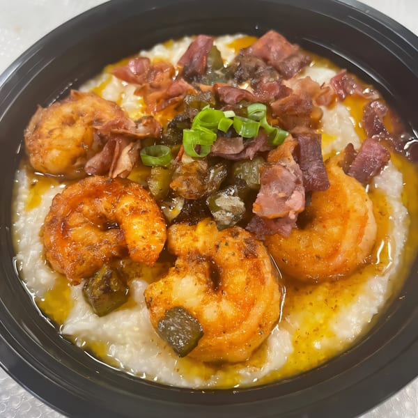 Noonie's Place shrimp and grits with bacon, okra, and green onions in a black bowl.
