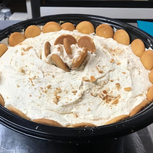 A large black bowl filled with Noonie's Place banana pudding, topped with vanilla wafers and crumbs.